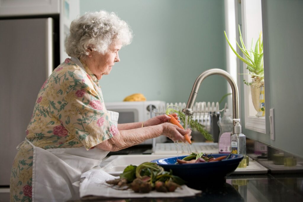 senior lady cleaning carrot on the sink